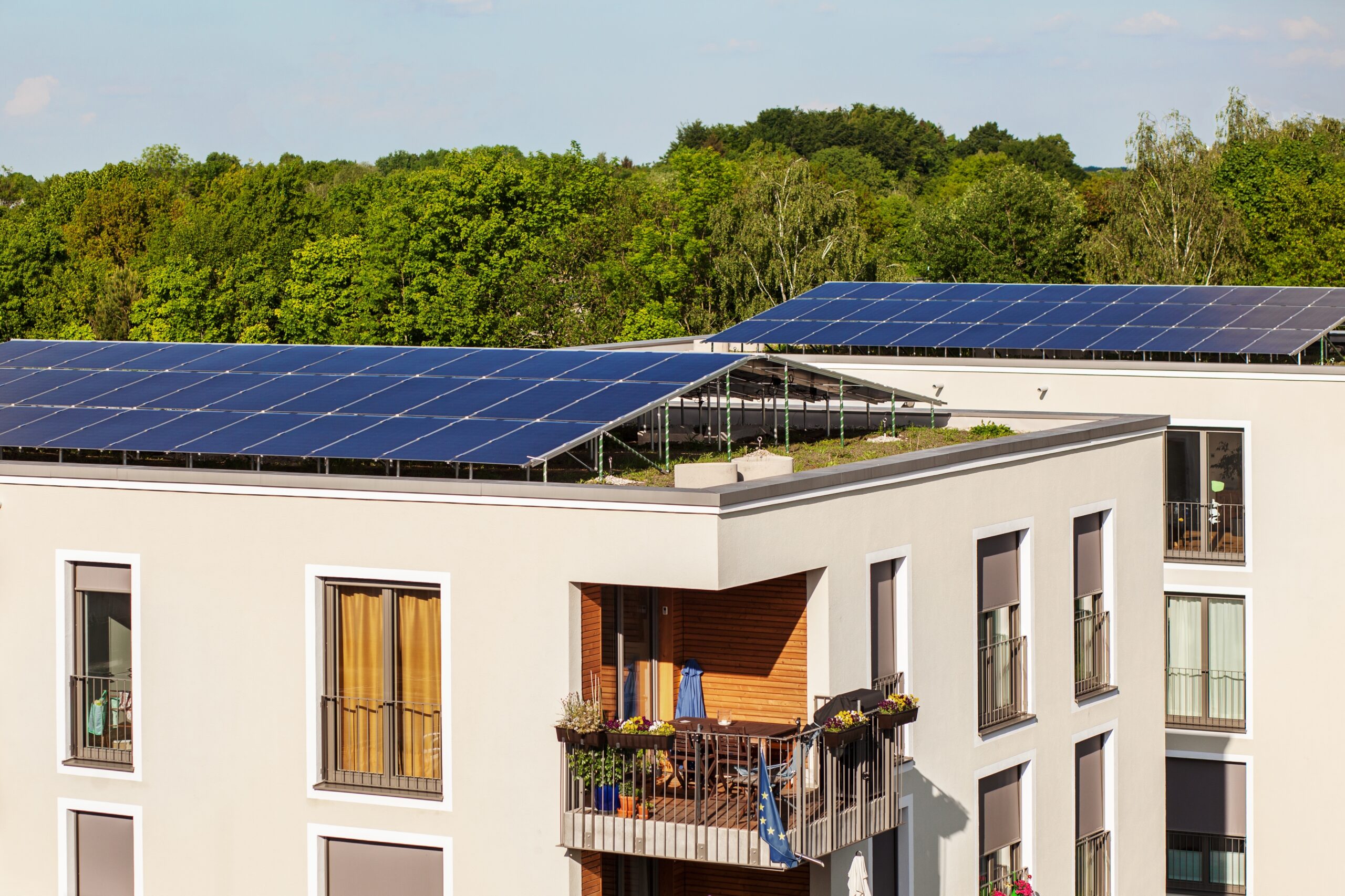 Modernes Mehrfamilienhaus mit Photovoltaikanlage und Gründach als Symbol für den klimafreundlichen Neubau KFN.