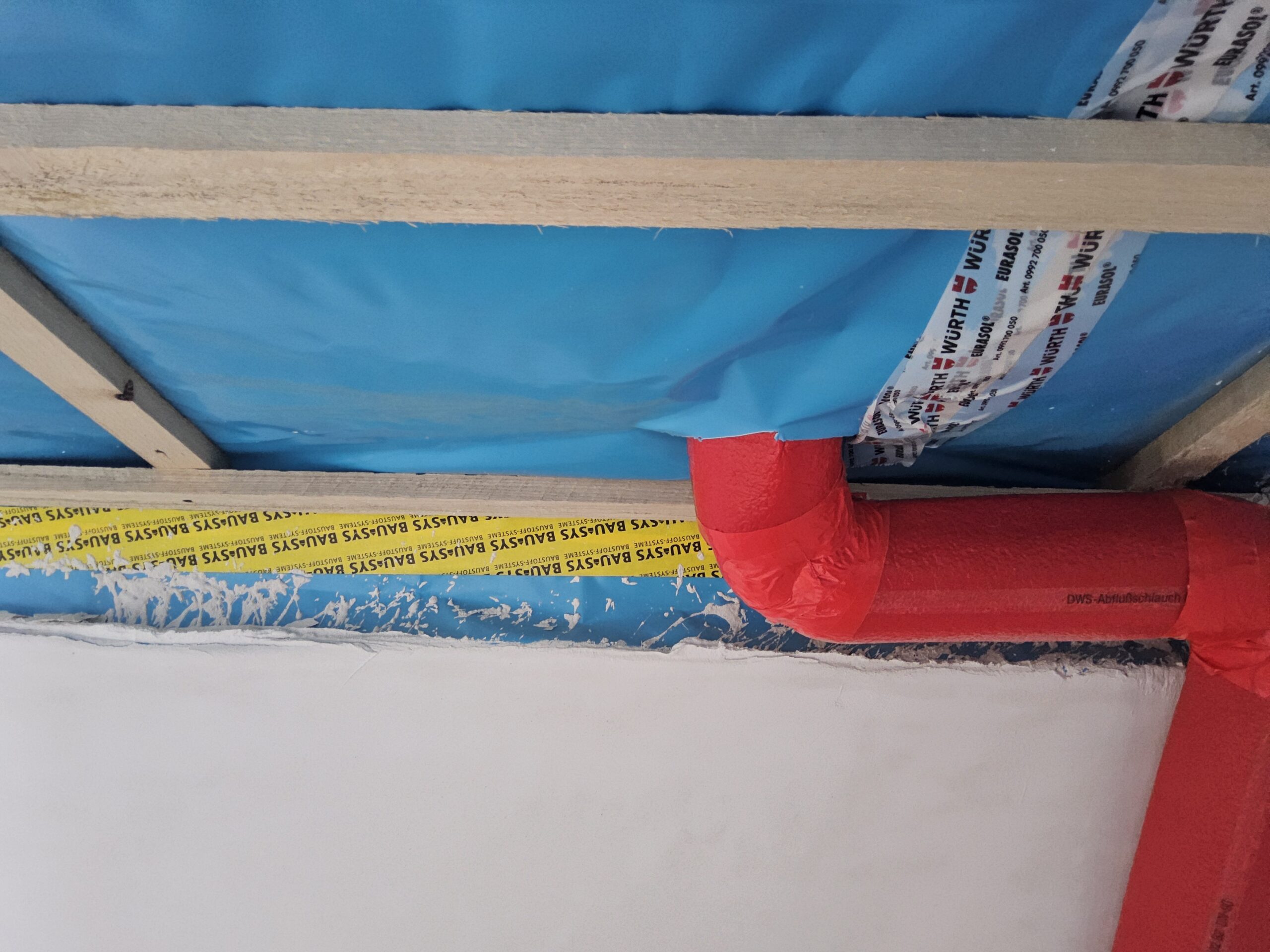 Detailaufnahme einer nicht fachgerecht verklebten blauen Dampfbremse mit gedämmten Sanitärleitungen im Innenausbau.